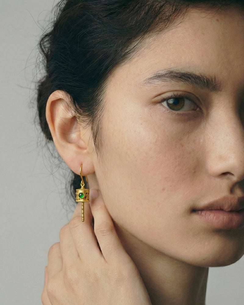 Gold kinetic drop earrings with a rotating openwork cylinder and a green jade element, on ear hooks