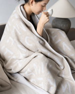 Woman wrapped in oat cashmere blanket sipping from cup
